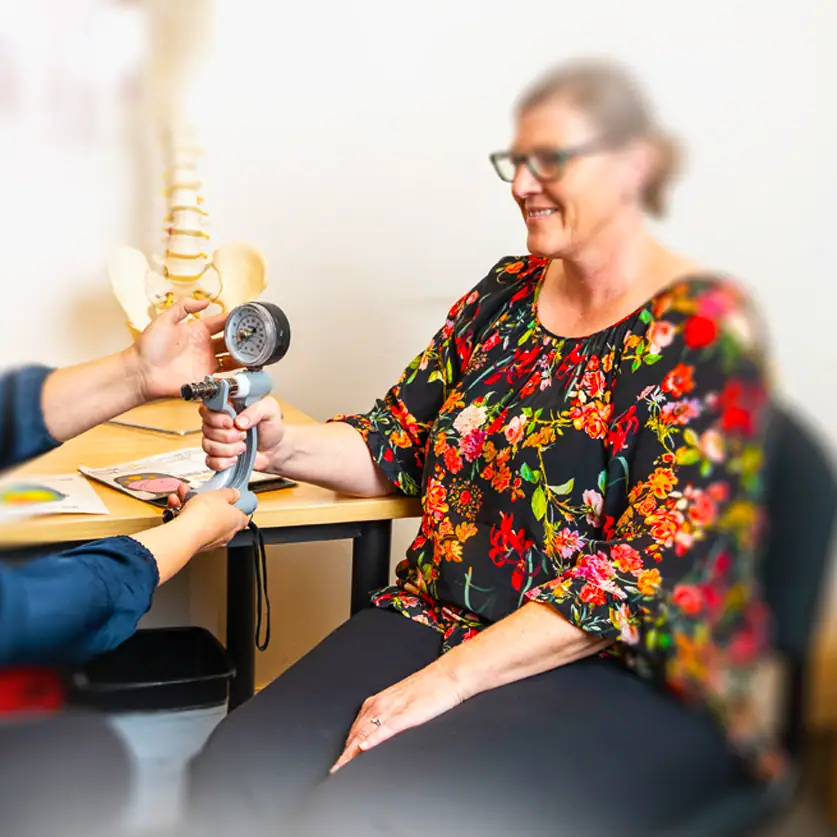 Healthcare professional assessing a woman's shoulder with a medical device in a clinic.